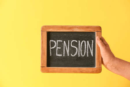 Hand of senior woman holding chalkboard with word PENSION on color backgroundの写真素材