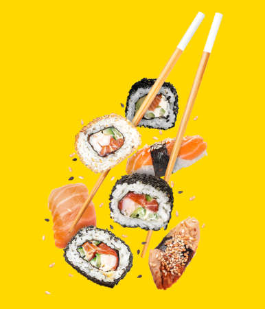 Flying chopsticks with tasty sushi on color backgroundの写真素材
