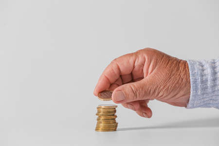 Hand of senior woman with coins on light background. Concept of pensionの写真素材