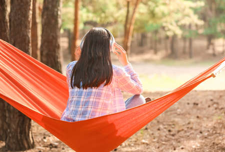 Young woman listening to music while relaxing in hammock outdoorsの写真素材