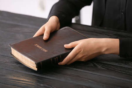 Man holding Holy Bible on wooden table