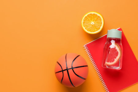 Bottle of clean water with grapefruit, orange, basketball and notebook on color backgroundの写真素材