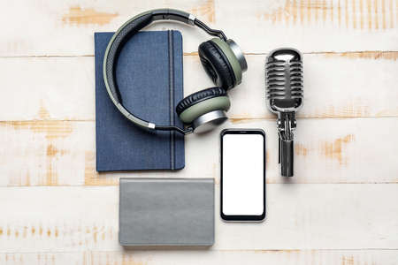 Headphones with microphone, mobile phone and notebooks on white wooden backgroundの写真素材
