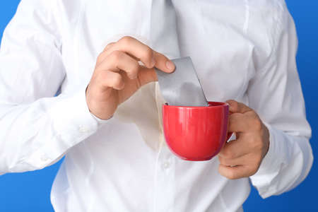 Young man with coffee stains on his shirt and tie in cup on color background