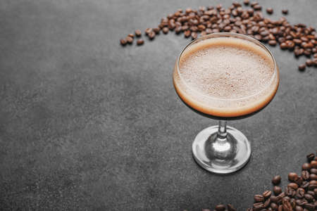 Glass of tasty espresso martini cocktail and coffee beans on dark background