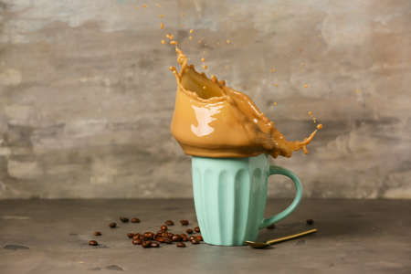 Cup of hot coffee with splash on gray background