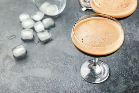 Two glasses of tasty espresso martini cocktail and ice cubes on table
