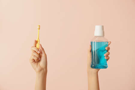 Female hands with tooth brushes and mouth rinse on color backgroundの写真素材