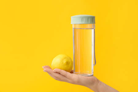Female hand, bottle of water and lemon on color background