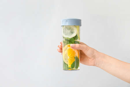 Female hand and bottle of mint infused water with citruses on light background