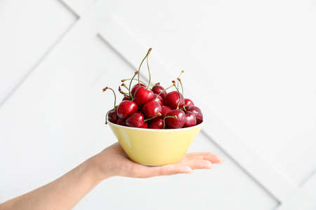Female hand with bowl of tasty cherry on light backgroundの写真素材