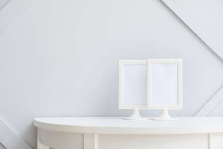 Blank photo frames on table near light wallの写真素材