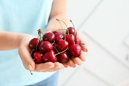 Woman with tasty cherry on light background