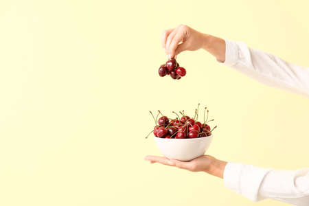 Female hands with bowl of tasty cherry on color backgroundの写真素材