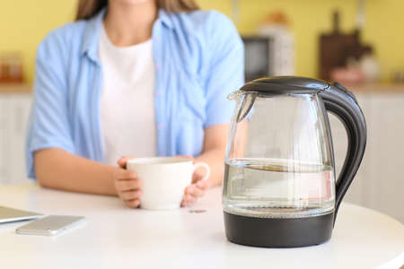 Electric kettle and woman with cup in kitchen, closeupの写真素材