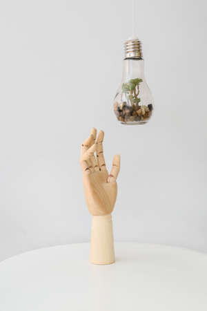 Wooden hand with decorative incandescent lamp on light background