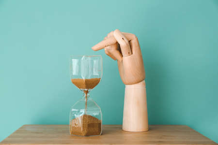 Wooden hand pointing at hour glass on tableの写真素材