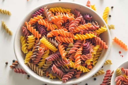 Bowl with uncooked pasta on light background
