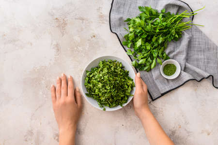 Female hands with fresh and dry parsley on light background