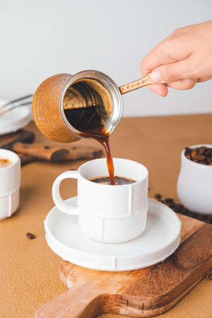 Woman pouring hot coffee from pot into cup on tableの写真素材