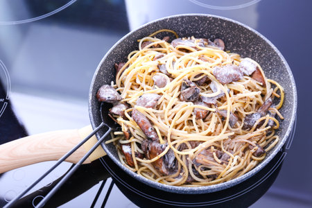 Frying pan with tasty pasta and mushrooms on stoveの写真素材