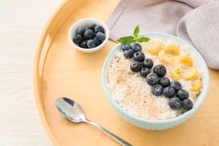 Bowl of tasty rice pudding with blueberry and cashew on wooden trayの写真素材