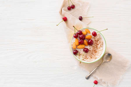 Bowl of tasty rice pudding with cherry and nuts on light tableの写真素材