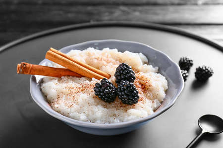 Plate of tasty rice pudding with blackberry and cinnamon on black trayの写真素材