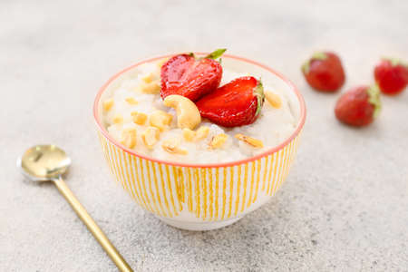 Bowl of tasty rice pudding with strawberry and nuts on light tableの写真素材