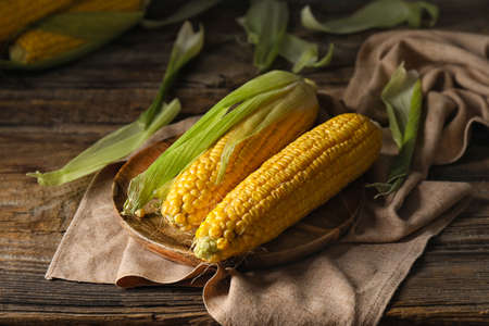Plate with fresh corn cobs on table