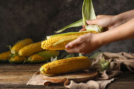 Woman with fresh corn cobs on table