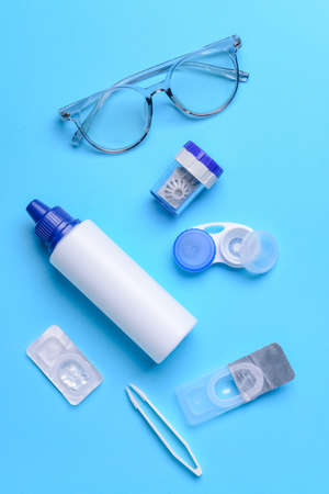 Containers with contact lenses, solution tweezers and eyeglasses on color background
