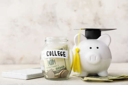 Piggy bank with graduation hat and jar with money for education on table. Tuition fees conceptの写真素材