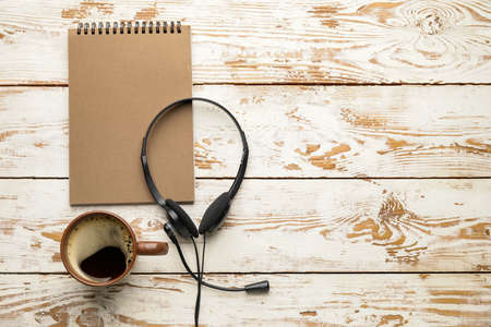 Headset with notebook and cup of coffee on white wooden backgroundの写真素材