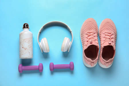 Sportive shoes, bottle of water, dumbbells and headphones on color backgroundの写真素材