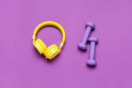 Dumbbells and headphones on color background