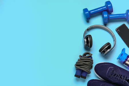 Sportive shoes, dumbbells, jumping rope and headphones on color background