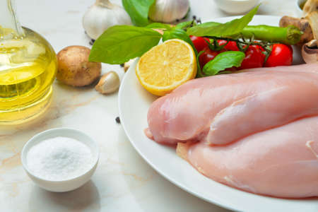 Plate with raw chicken fillet, herbs and vegetables on tableの写真素材