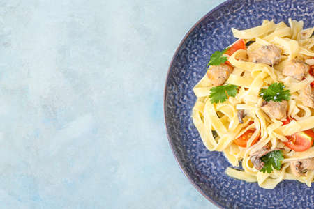 Plate of tasty pasta with chicken and cherry tomatoes on color tableの写真素材