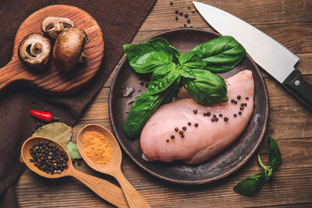 Plate with raw chicken fillet, black pepper and basil on wooden backgroundの写真素材