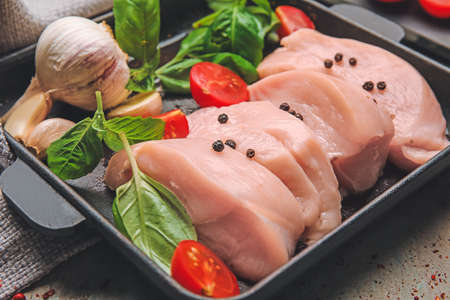 Ceramic plate with raw cut chicken fillet, tomatoes and basil on tableの写真素材