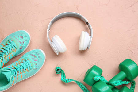 Sportive shoes, dumbbells, measuring tape and headphones on color background
