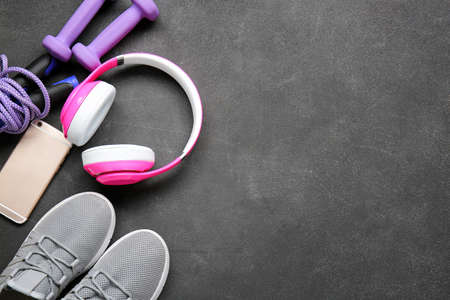 Sportive shoes, dumbbells, jumping rope, mobile phone and headphones on gray background