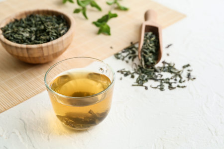 Cup of green tea and bowl with dry leaves on light tableの写真素材