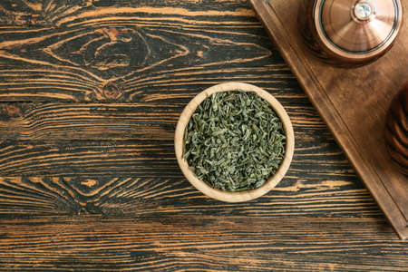Bowl with dry green tea on wooden table