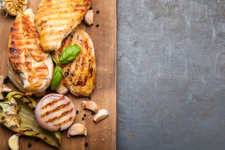 Board with cooked chicken fillet and vegetables on dark backgroundの写真素材