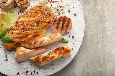 Board with cooked chicken fillet and vegetables on table