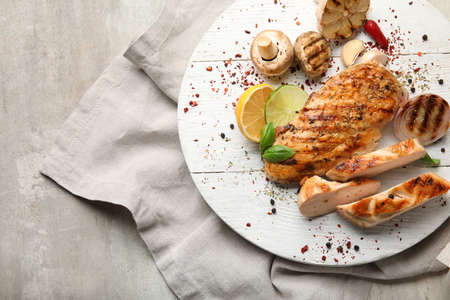 Board with cooked chicken fillet and vegetables on tableの写真素材