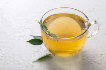 Cup of hot aromatic tea and green tea leaves on tableの写真素材