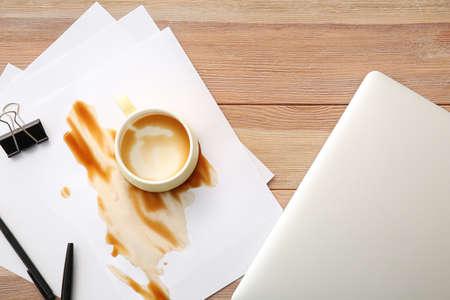 Laptop, stationery and spilled coffee on office tableの写真素材